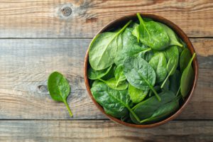 Spinach in a brown bowl on wood surface