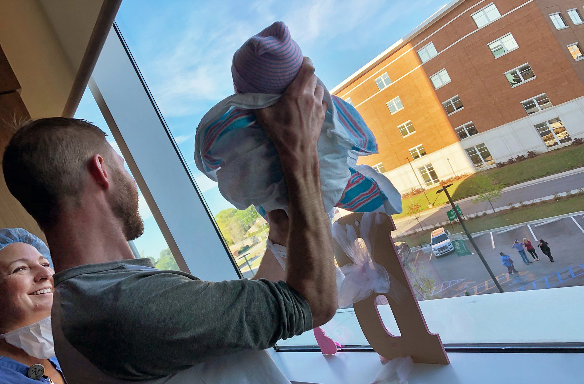 Father holding baby up to window for family to see