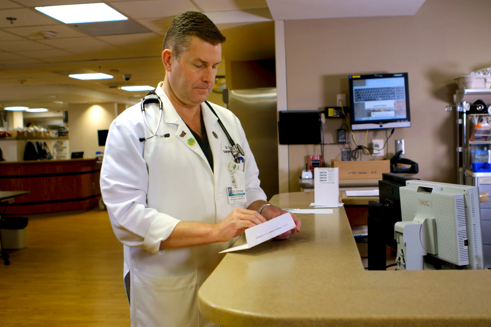 Dr. Todd Crump at work, standing at the clinic desk reading a medical pamphlet.
