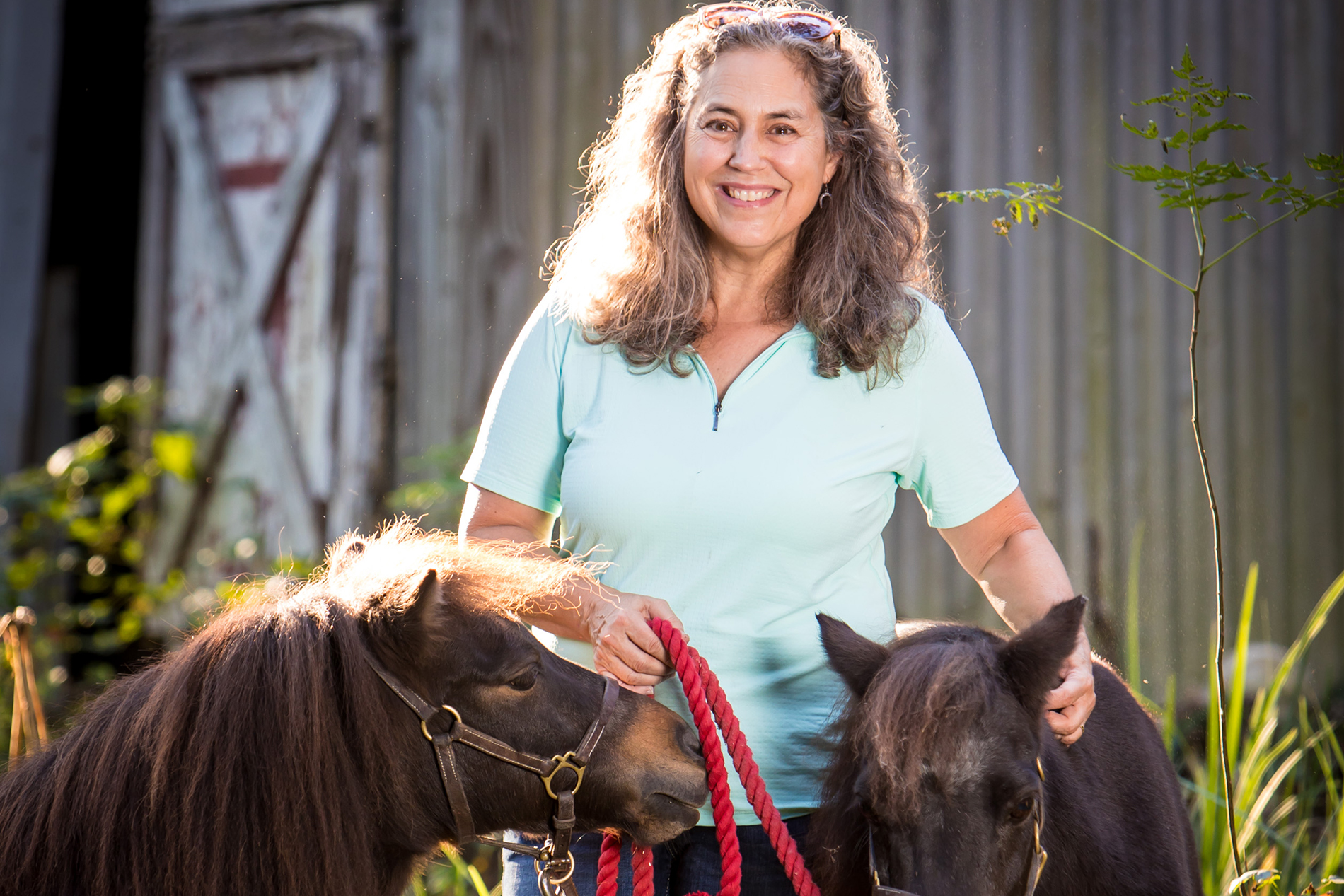 Betsy Schindler by barn with two ponies