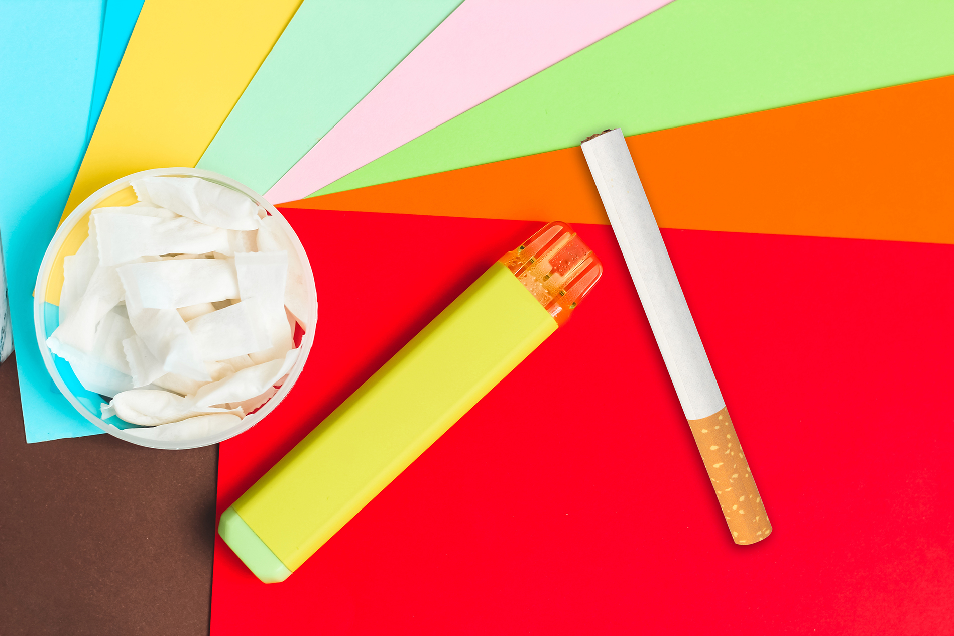 Cigarette, vape and nicotine pouches laying on a colorful background