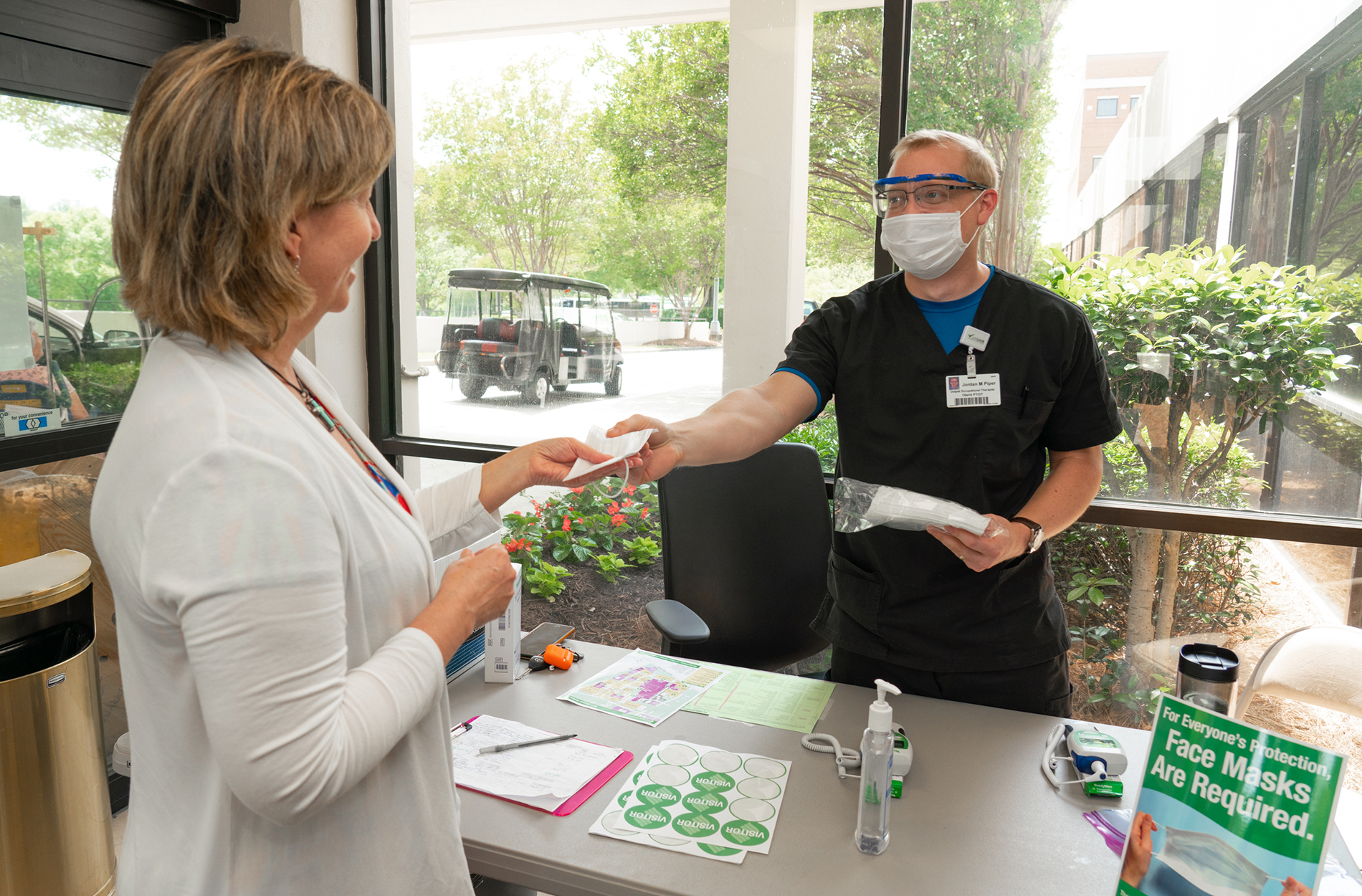 COVID Visitation Hospital employee handing visitor a mask at hospital entrance