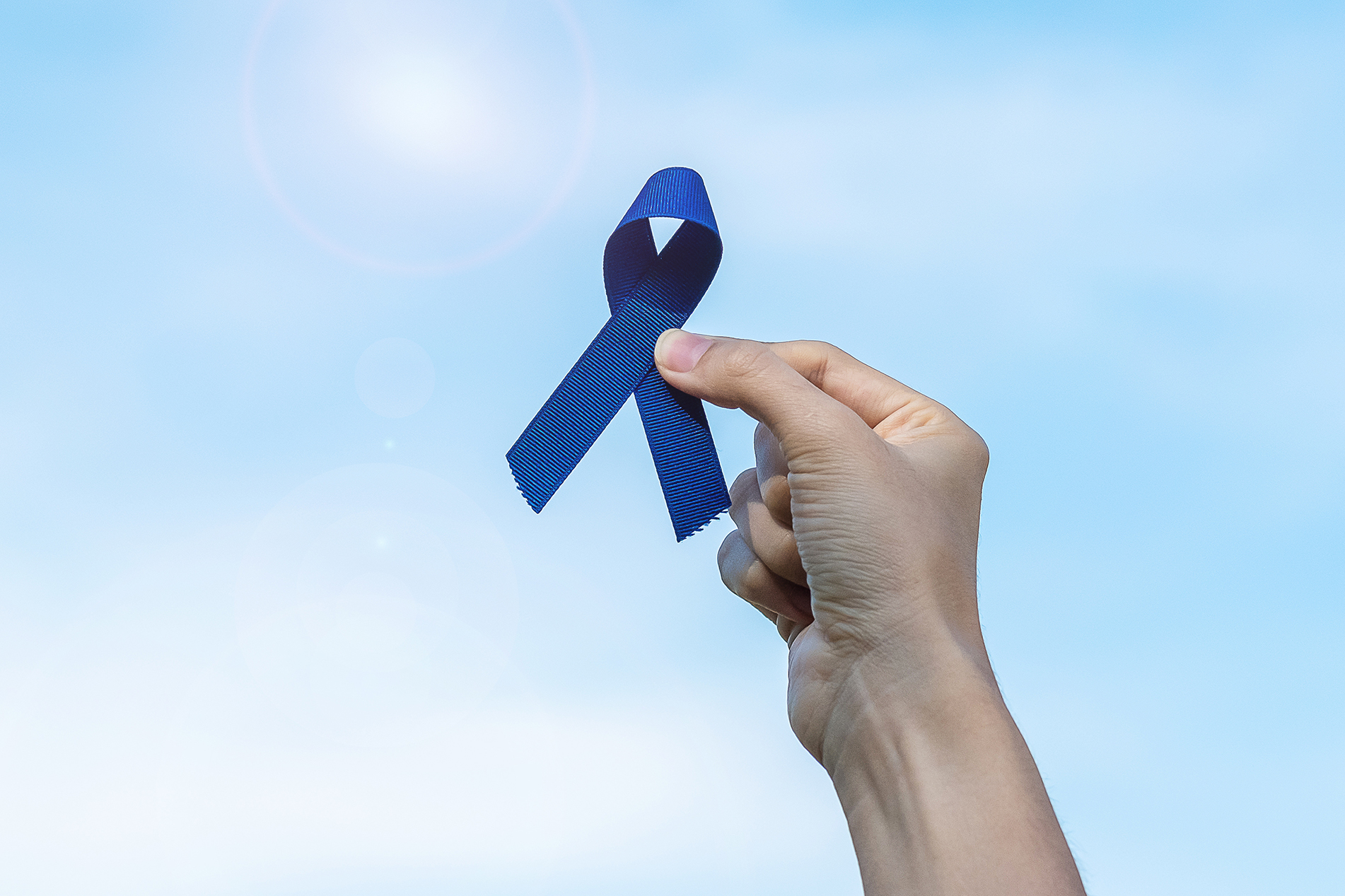 Woman's hand holding blue ribbon up toward the sky