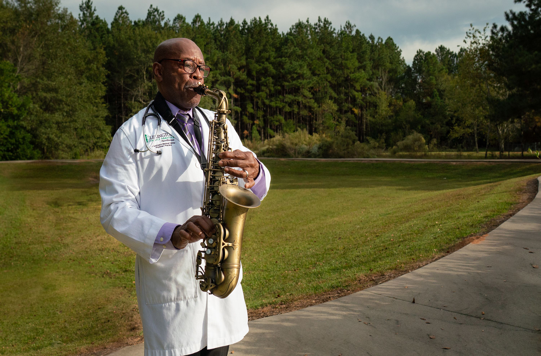 Dr. Marion playing saxophone outside wearing his white lab coat