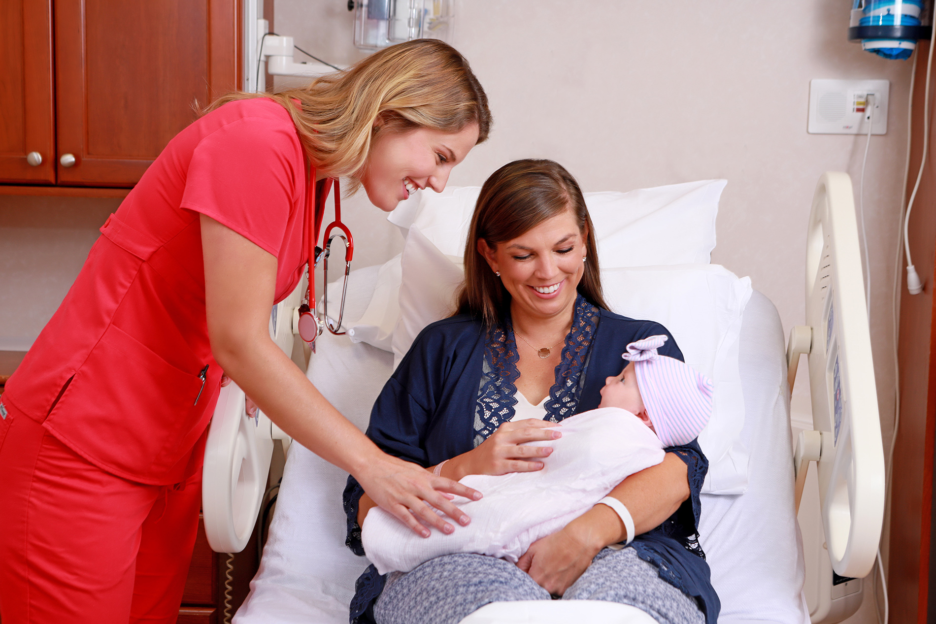 Mother holding newborn baby with nurse looking on