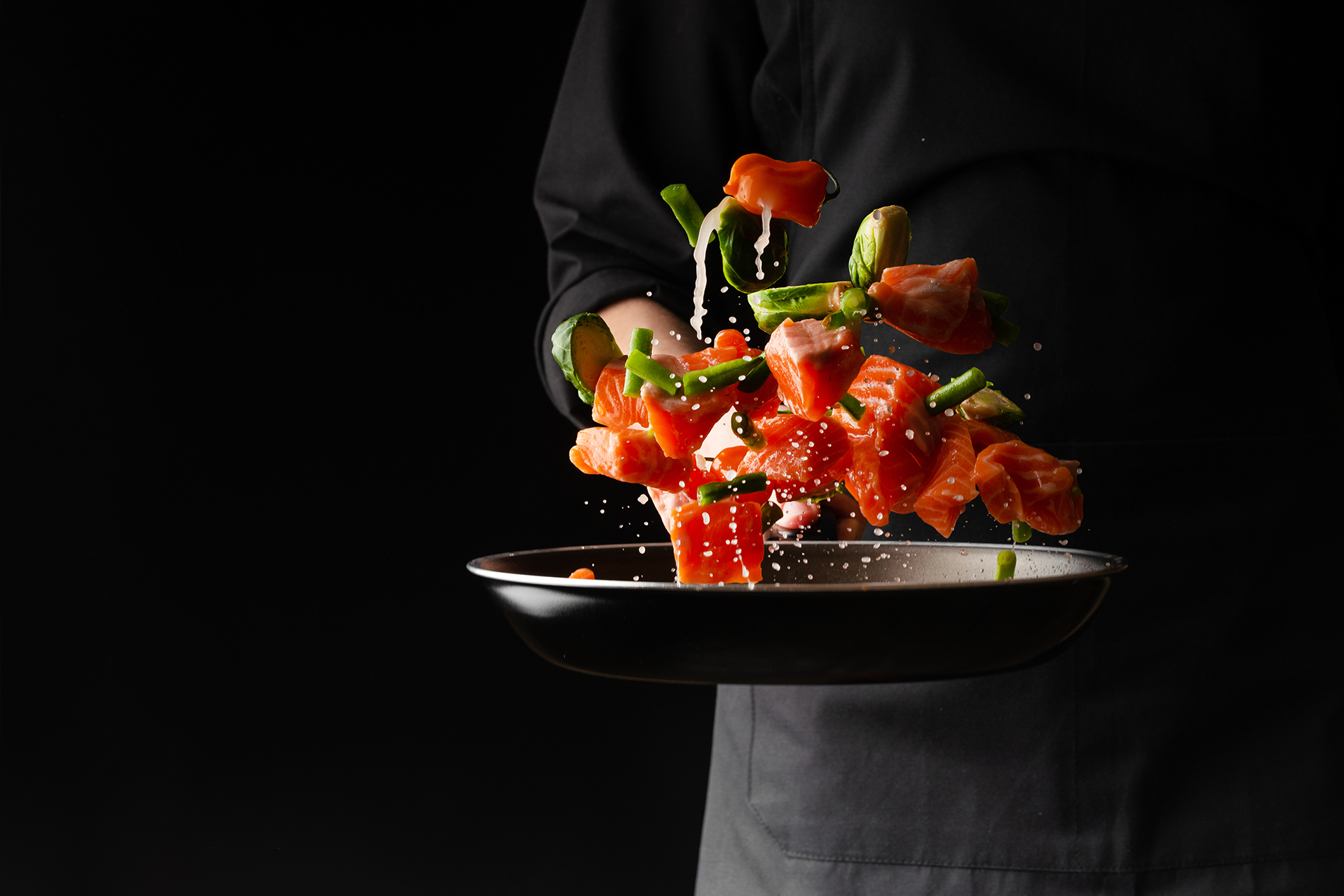 Chef tossing raw salmon in pan
