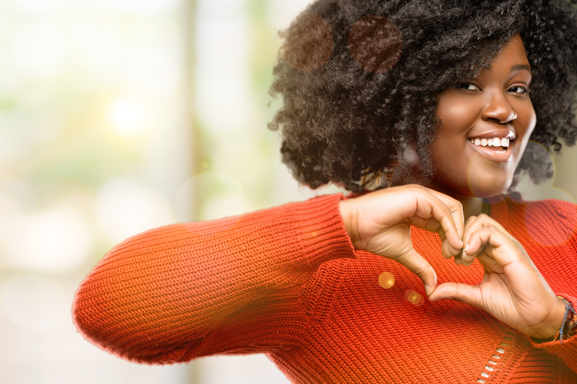 Smiling young black woman in red sweater making heart symbol with hands