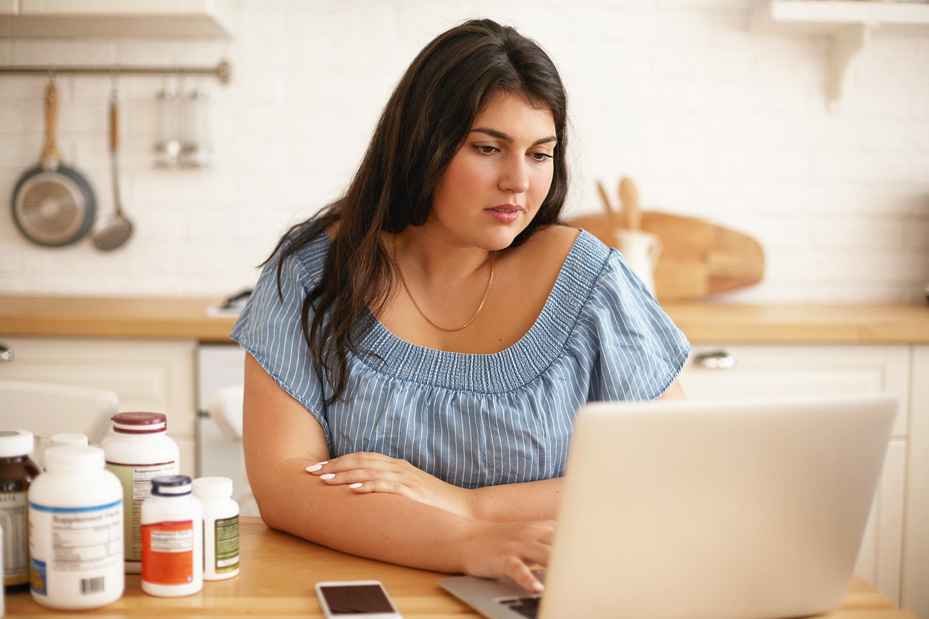 Overweight woman looking at laptop in her kitchen