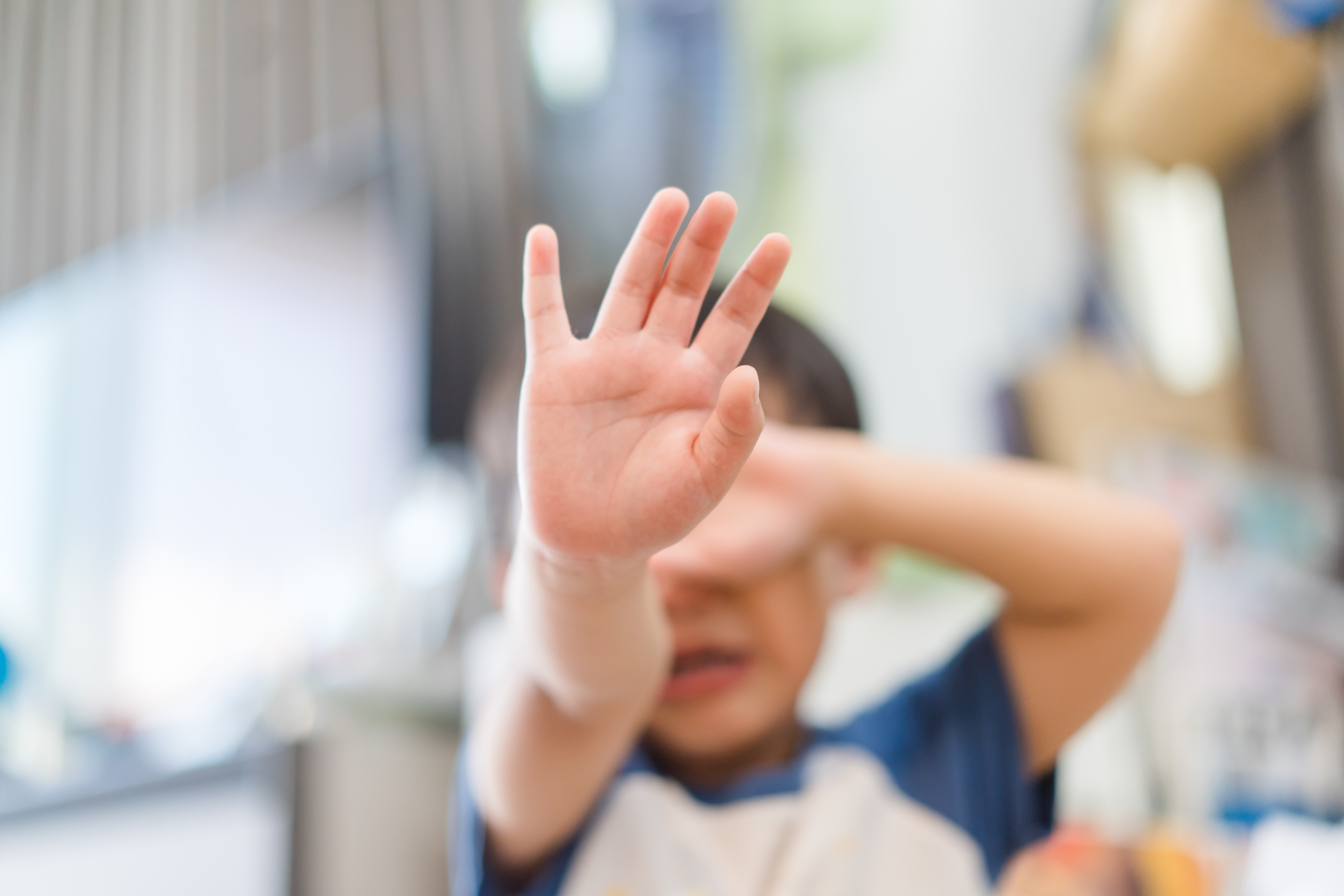 Upset young boy with one hand over his face and one hand forward to signal stop