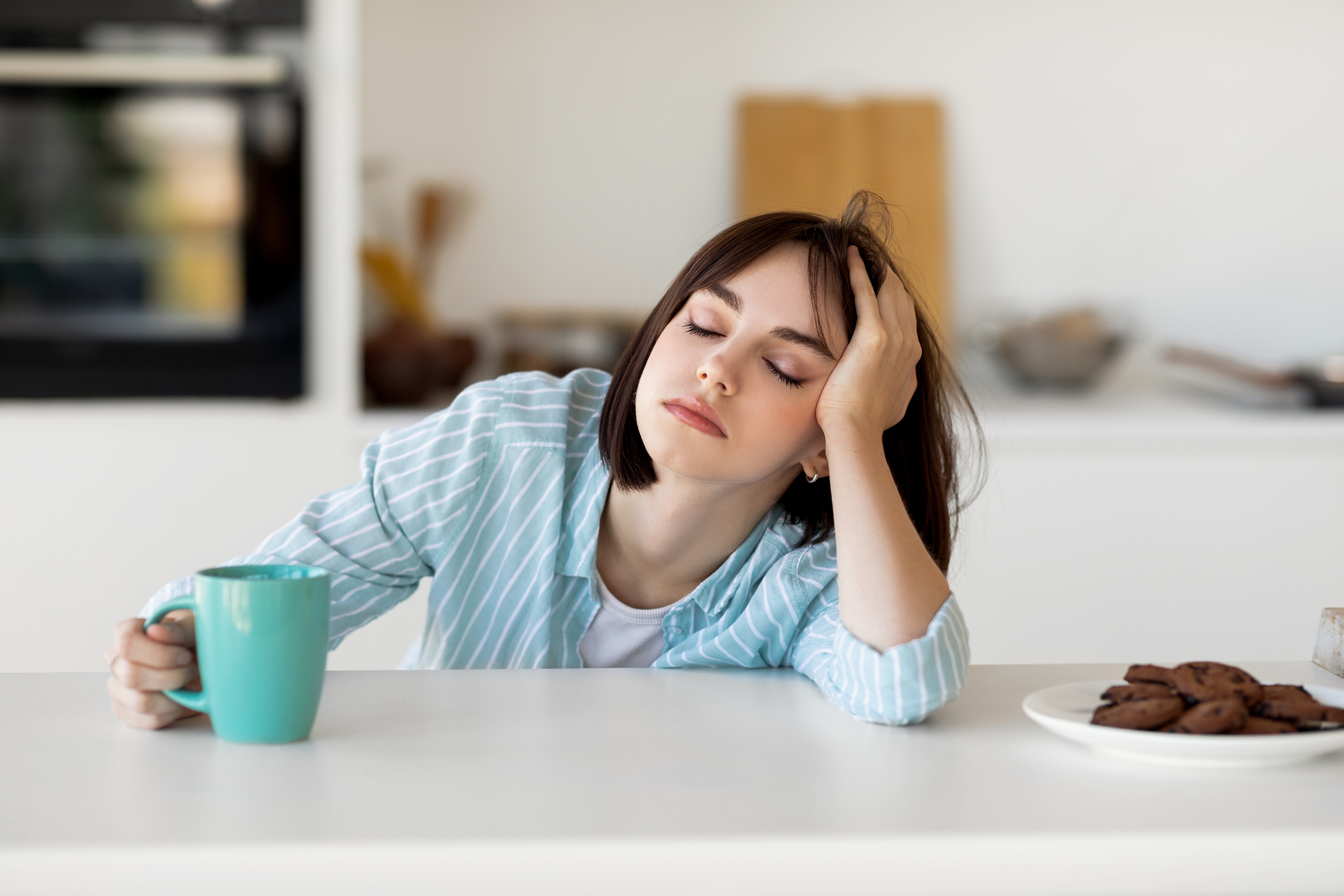 Tired woman with eyes closed at table in her kitchen