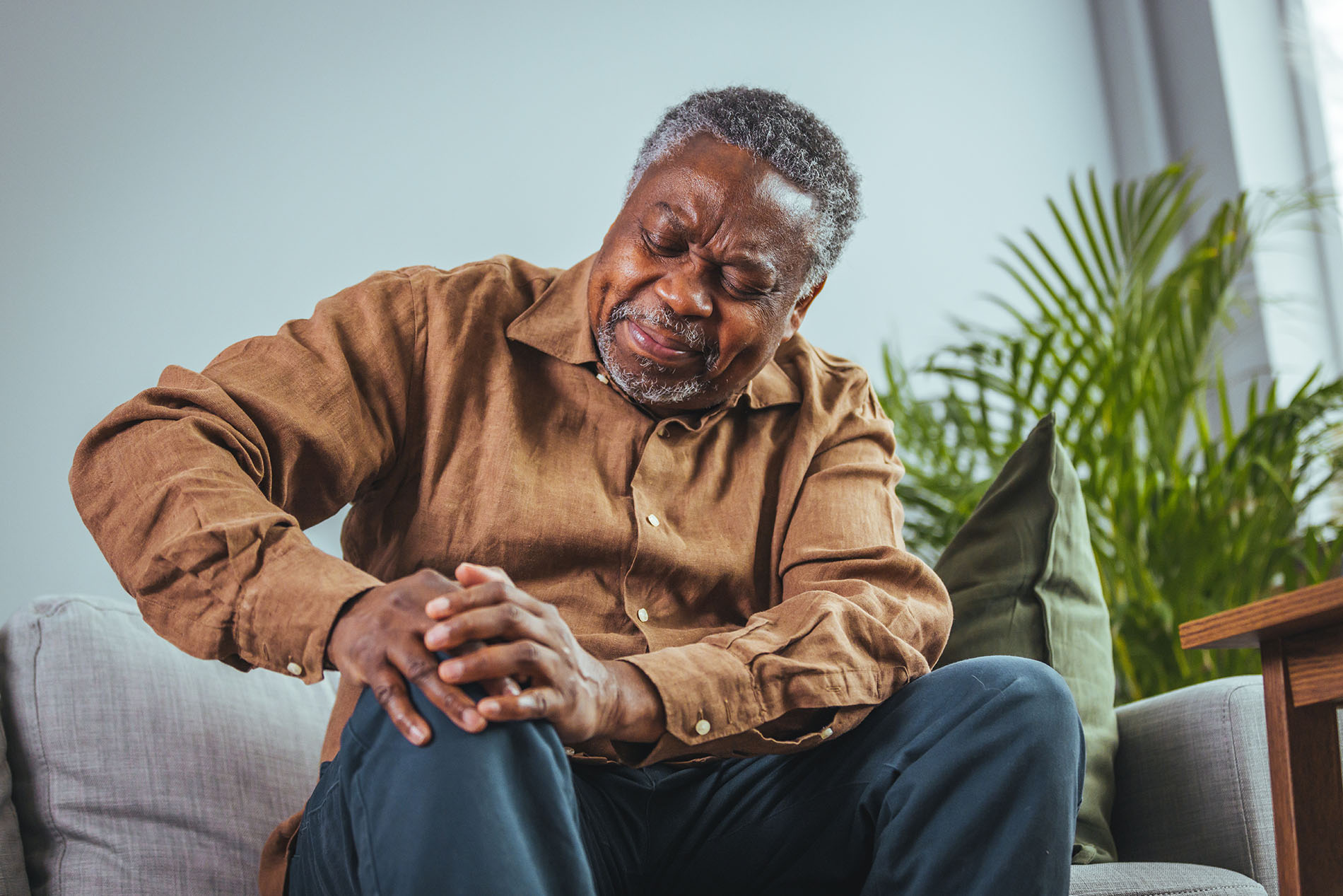 Older Black man sitting on couch touching his knee