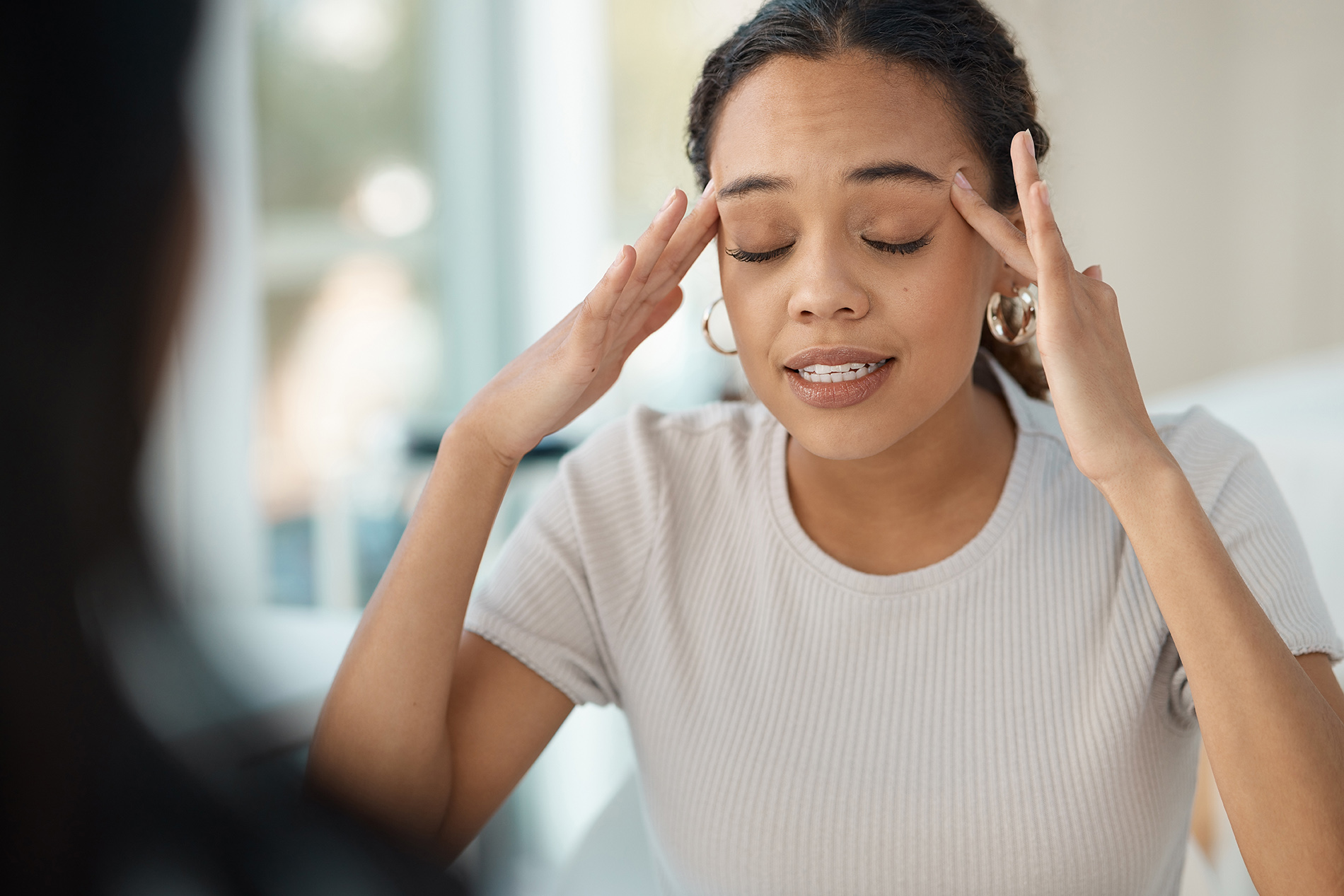 Young upset black woman talking to doctor while touching her temples