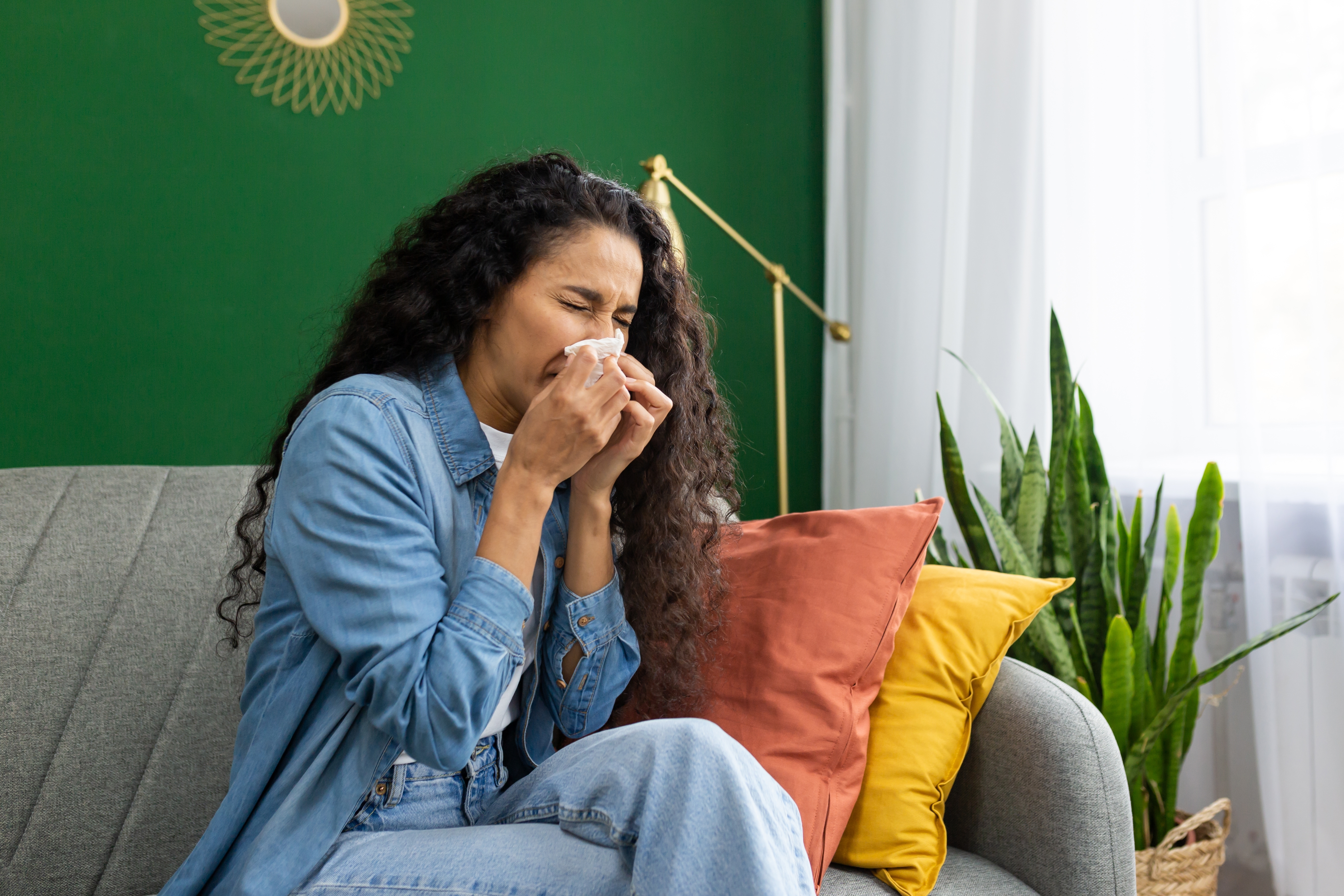 Woman sitting on couch blowing her nose