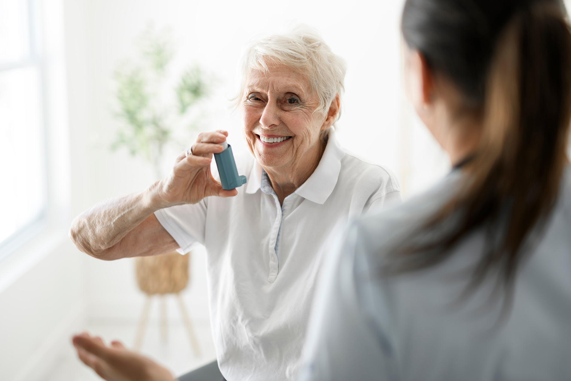 Older woman holding an inhaler and smiling at a nurse