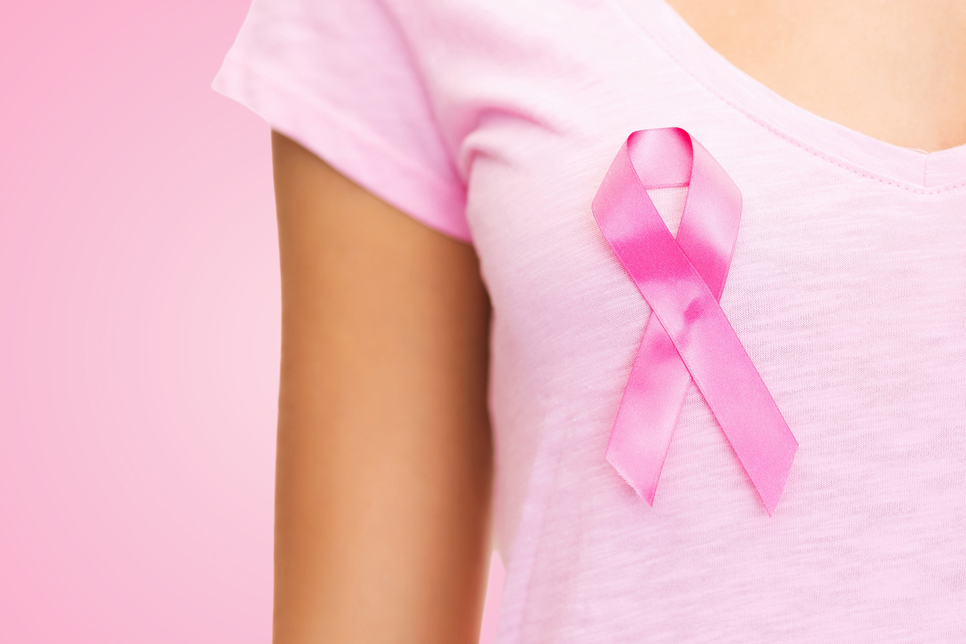 Neck and chest of young woman in pink tshirt with pink ribbon pinned to her shirt