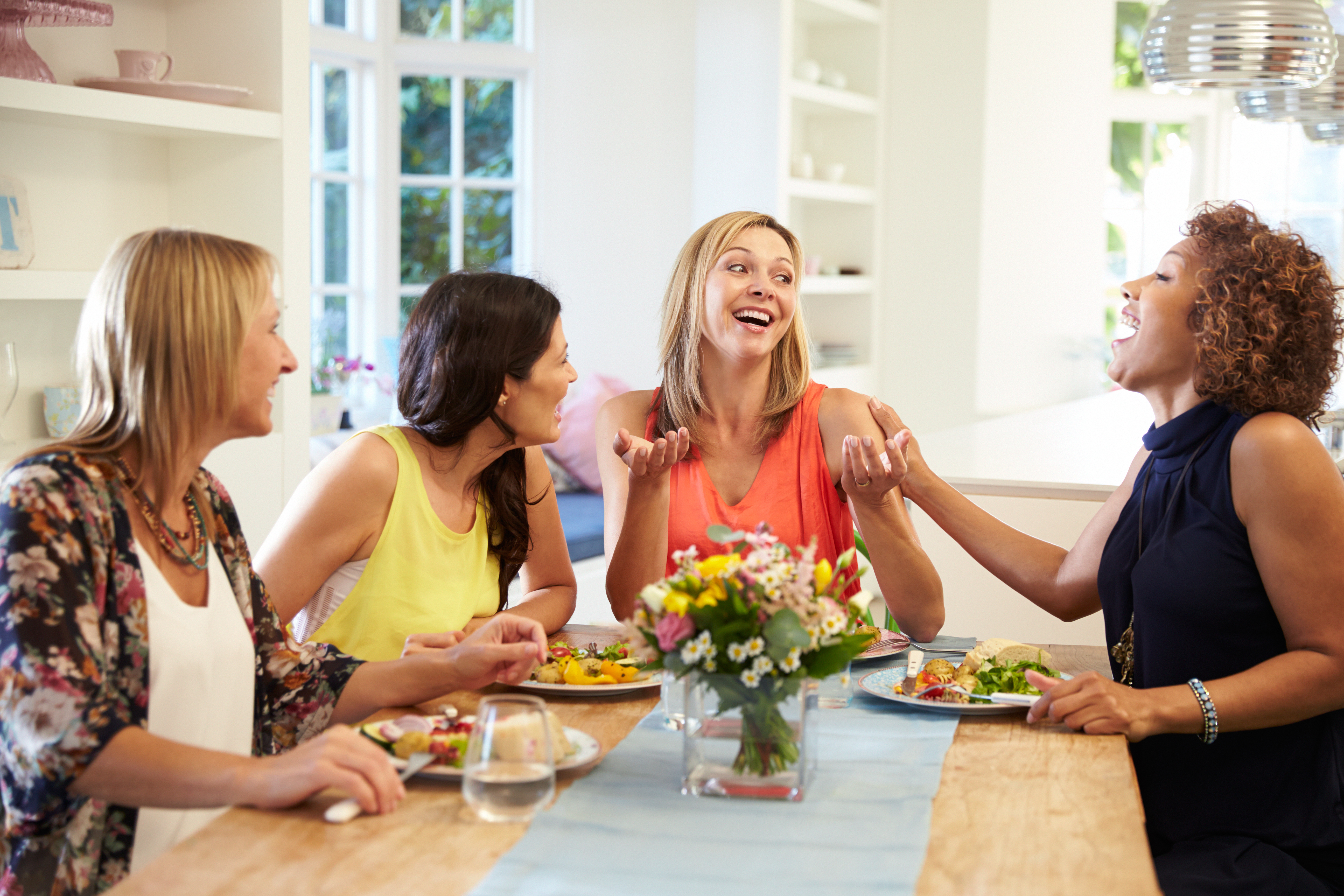 Group of middle ages women laughing around a dining table