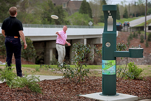 Men playing frisbee by Gibson Pond Park water fountain 