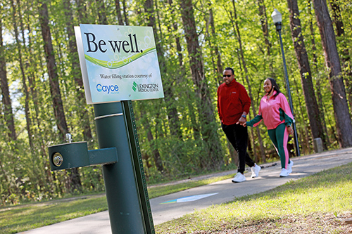 Couple walking by Be Well water fountain on Timmerman Trail 